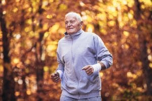 Senior runner in nature. Elderly sporty man running in forest during morning workout. Healthy and active lifestyle at any age
