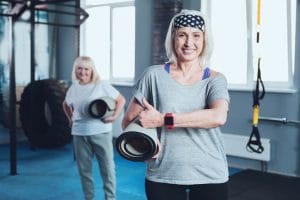 older woman with workout mat smiling