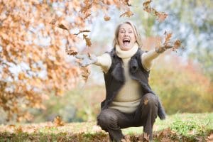 mature woman tossing autumn leaves in the air